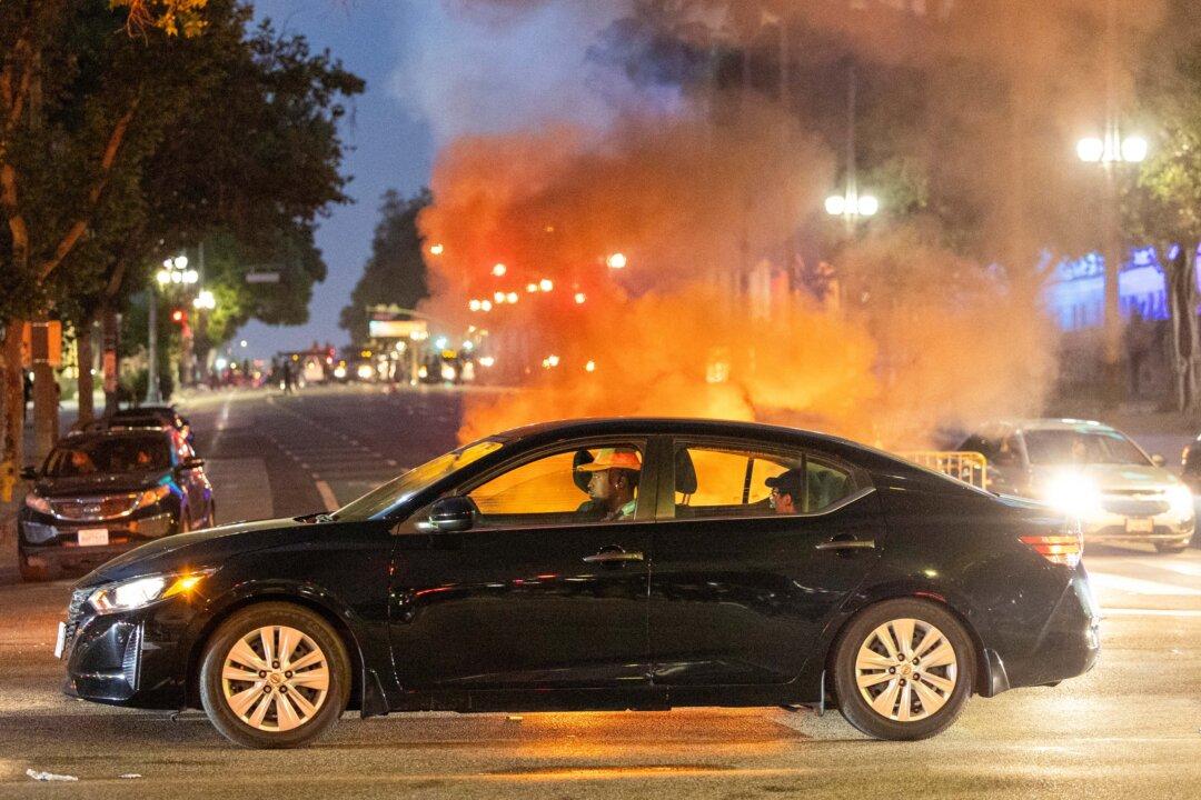 Occupants in a car drive past a fire amid clashes with law enforcement in the streets surrounding the federal building during a protest following federal immigration operations in Los Angeles on June 8, 2025. (Ringo Chiu/AFP via Getty Images)