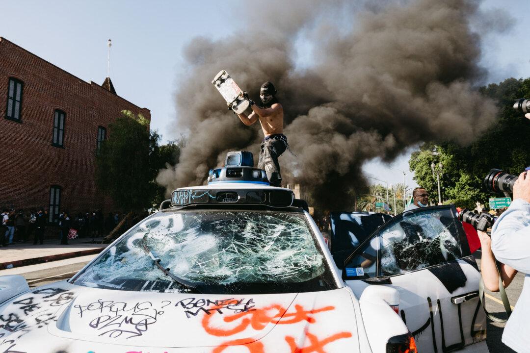 A protester attacks a Waymo vehicle with anti-ICE graffiti during demonstrations in Los Angeles on June 8, 2025. (David Pashaee/Middle East Images/AFP via Getty Images)