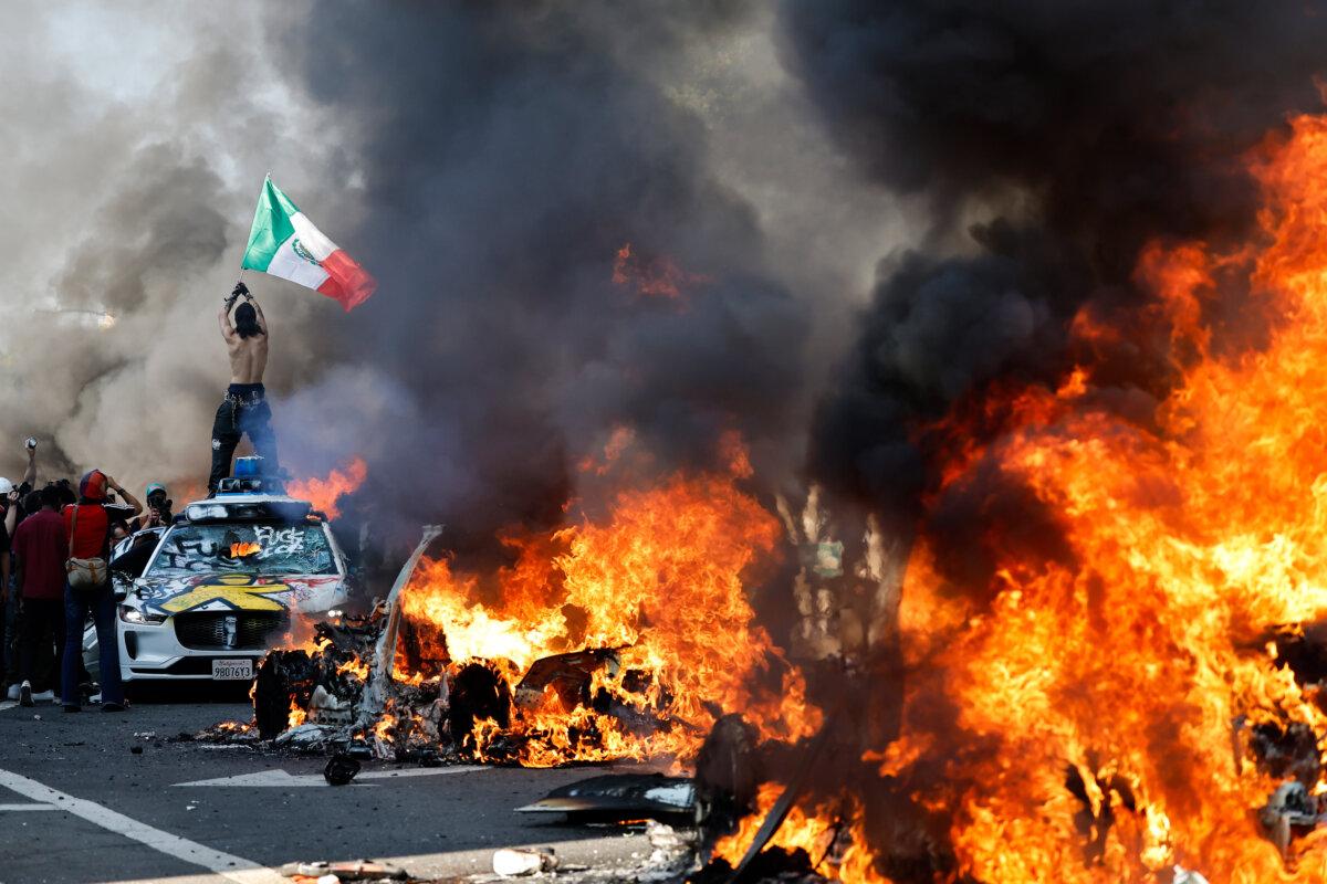 A protestor holds up a Mexican flag as burning cars line the street in Los Angeles, Calif., on June 08, 2025. (Mario Tama/Getty Images)