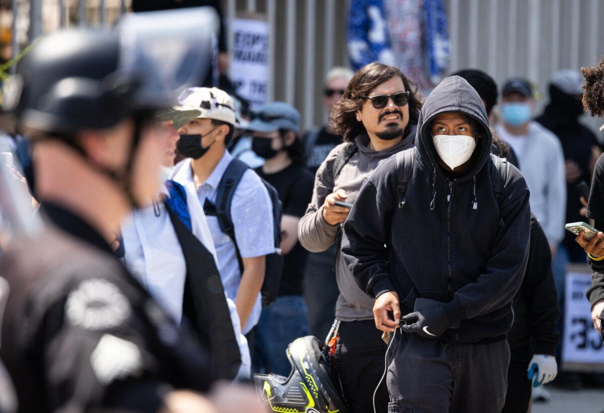 A man puts on gloves in front of a line of police officers in downtown Los Angeles on June 9, 2025. (John Fredricks/The Epoch Times)