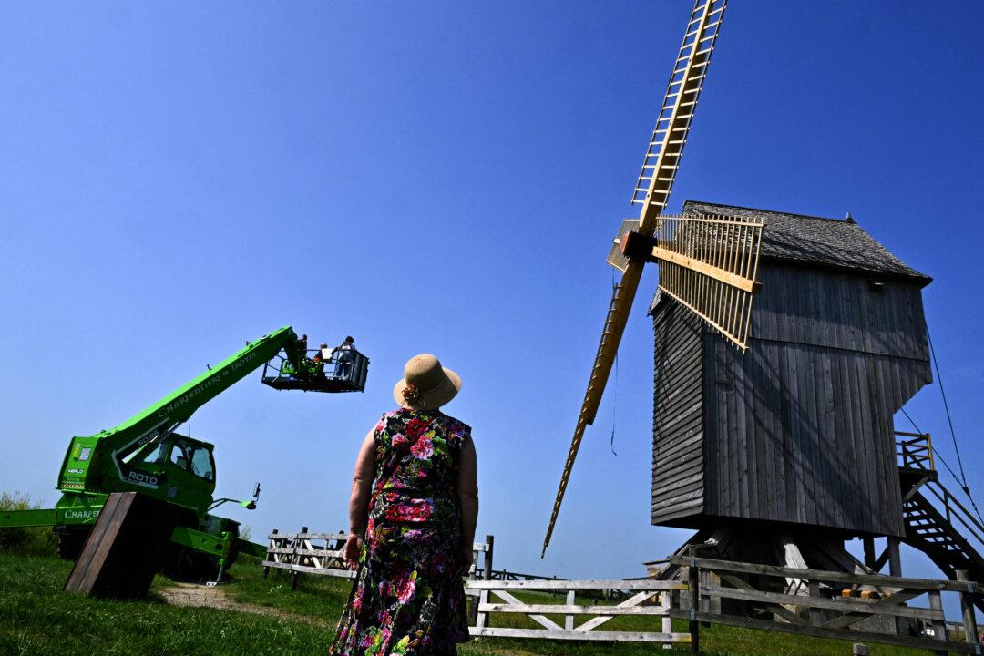 A woman looks at carpenters on a crane platform working to assemble the blades of the 'Moulin de Valmy' (Valmy windmill) after renovation following damage caused by a storm in 2022, in Valmy, France, on June 12, 2025. The Moulin de Valmy became a symbol of the French Republic following the battle of Valmy in 1792. The battle was the first victory of France against the Prussian army and led to the creation of the French Republic. (Francois Nascimbeni/AFP via Getty Images)
