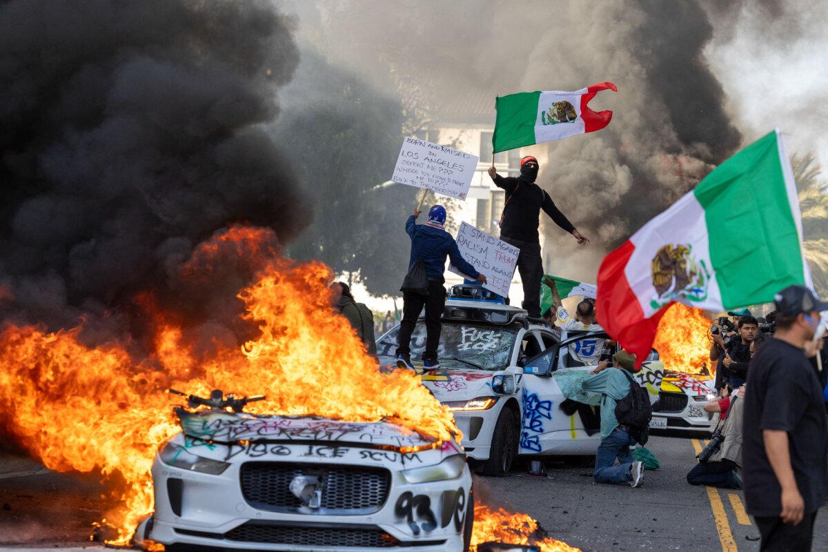 Protesters wave flags amid wrecked and burning Waymo vehicles as they clash with law enforcement near the federal building in Los Angeles on June 8, 2025. (Ringo Chiu/AFP via Getty Images)