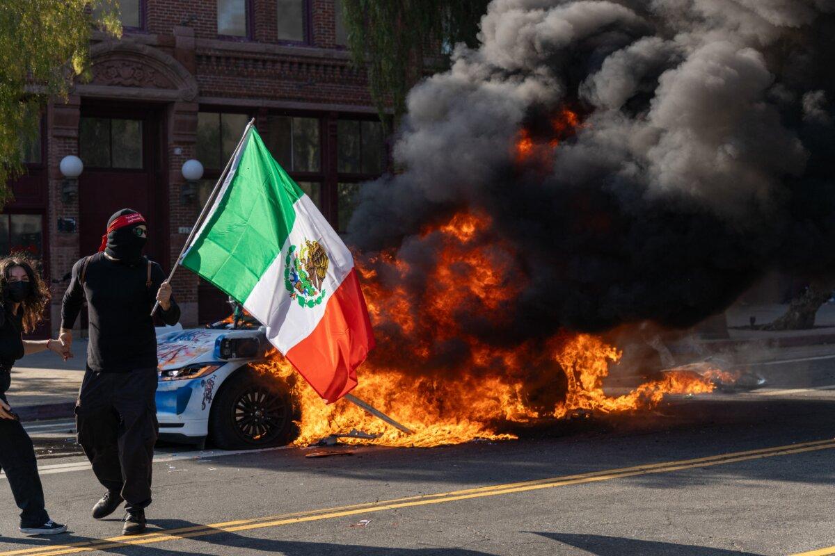 A demonstrator waves a Mexican flag in front of a burning vehicle during a protest in Los Angeles on June 8, 2025. (Lauren Puente/Middle East Images via AFP)