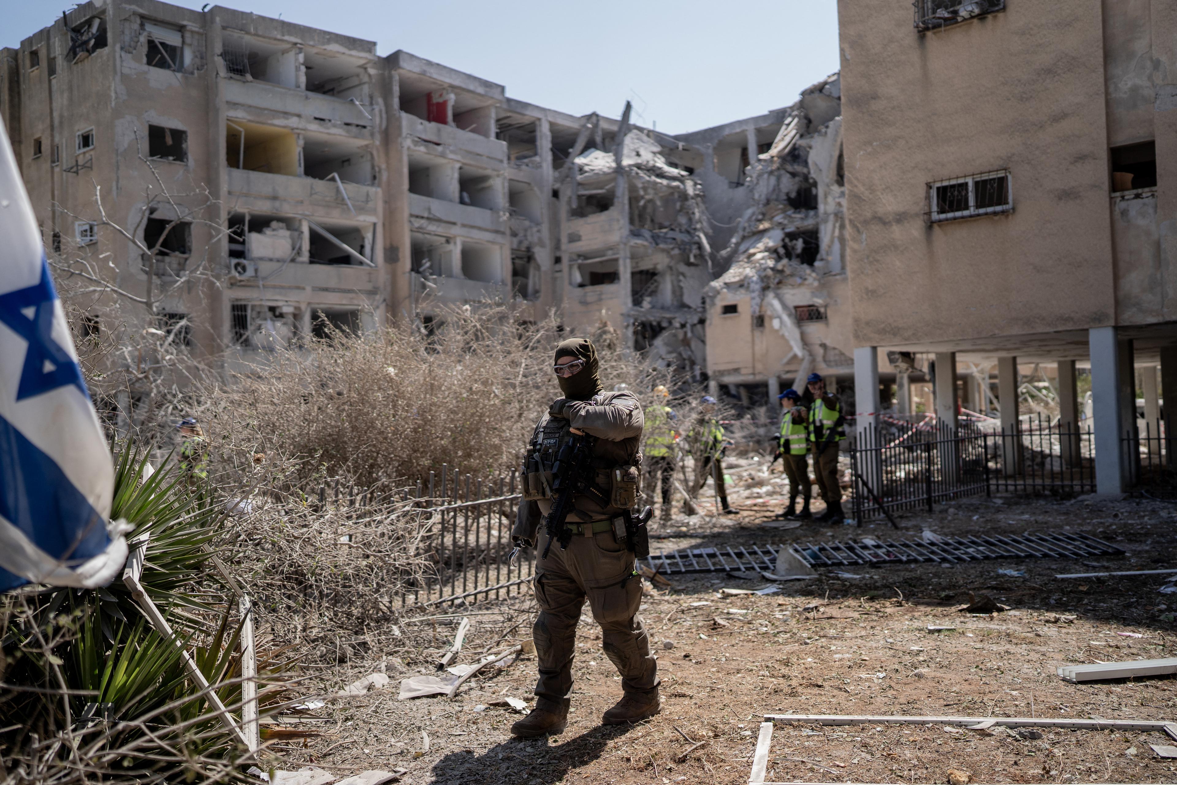 A masked Israeli policeman stands guard outside damaged buildings in Holon, Israel, on June 19, 2025. (Dima Vazinovich / Middle East Images via AFP)
