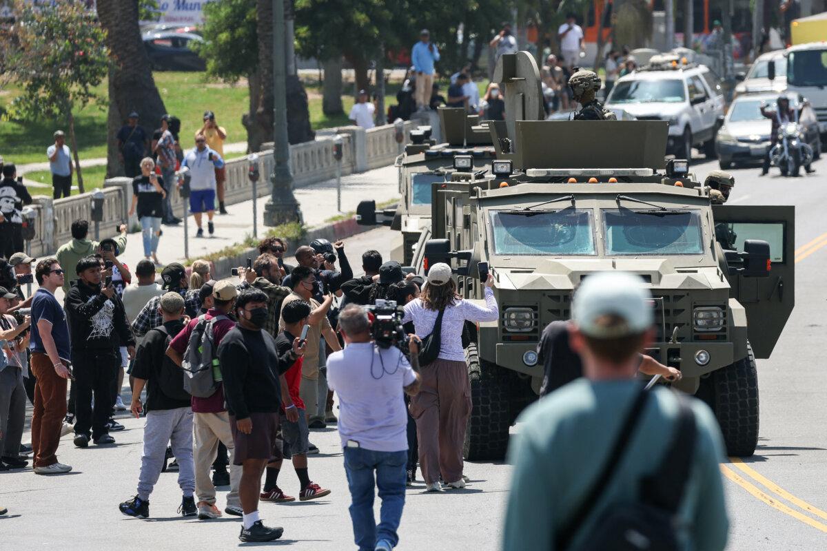 People watch Customs and Border Protection agents ride an armored vehicle along Wilshire Boulevard near MacArthur Park in Los Angeles on July 7, 2025. (Patrick T. Fallon/AFP via Getty Images)