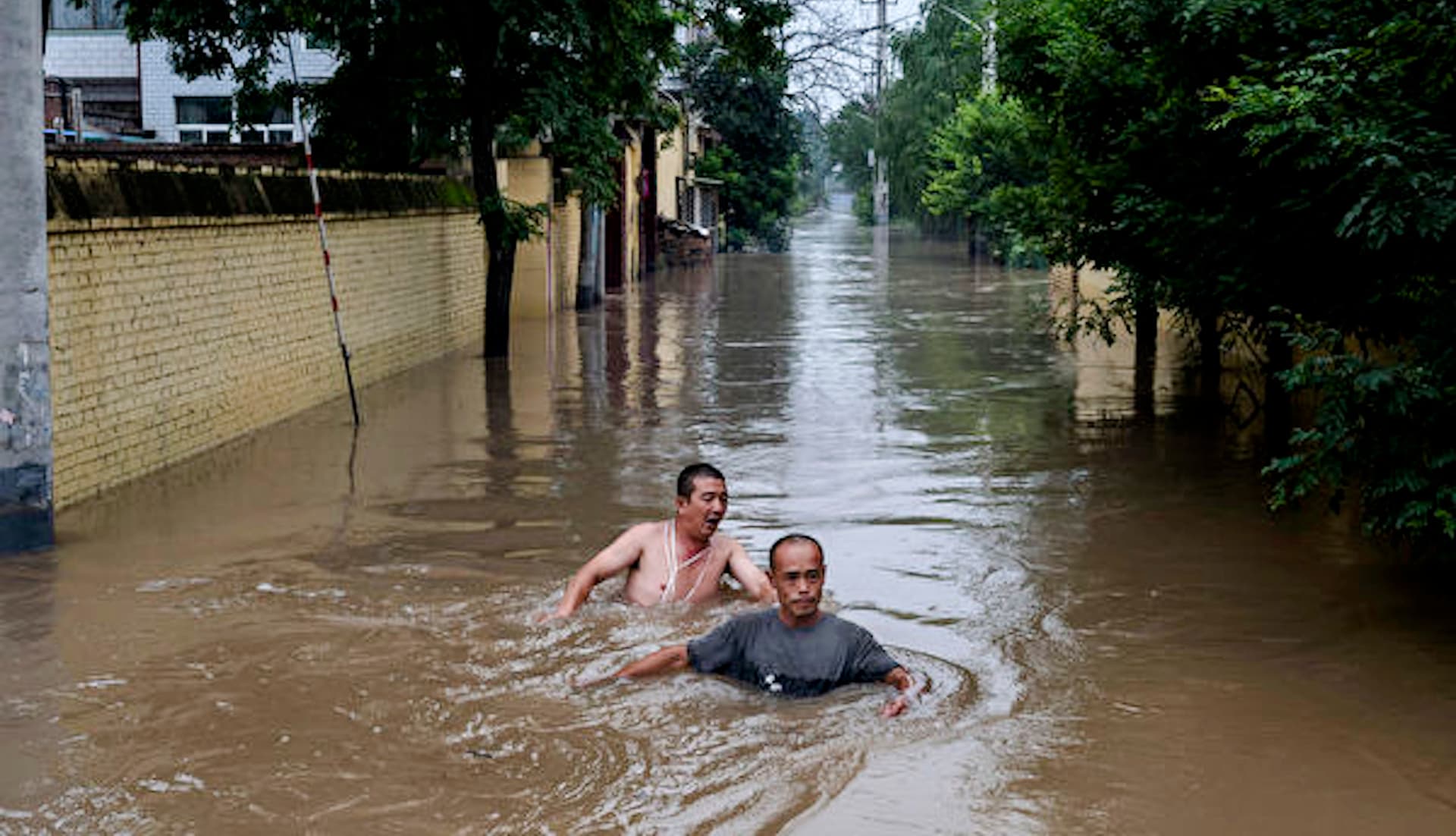 Local residents struggle in deep, fast-moving water as they make their way toward rescuers in a boat in a flooded area near Zhuozhou, Hebei Province, south of Beijing, on Aug. 3, 2023. (Kevin Frayer/Getty Images)