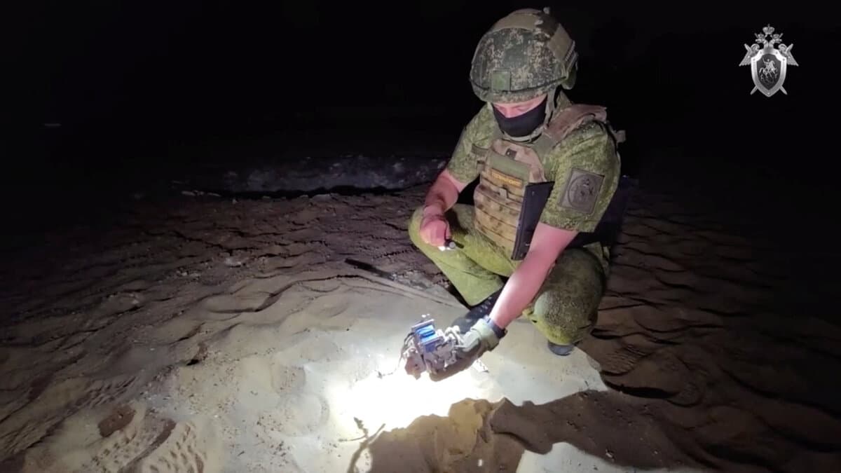 An officer of the Russian Investigative Committee examines remains of a drone on a beach following what local authorities called a Ukrainian drone attack, in this still image from a video released on July 9, 2025. (Russian Investigative Committee/Handout via Reuters)