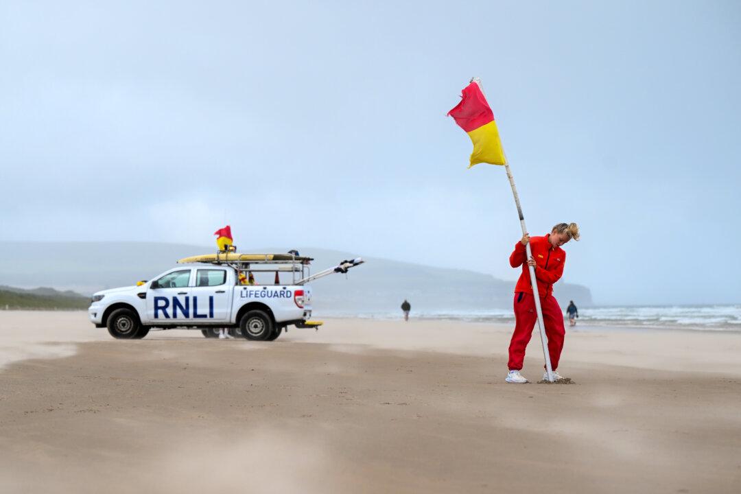 An RNLI lifeguard battles strong winds on Portstewart Strand as she plants a warning flag advising swimmers against entering the water in Portstewart, England, on Aug. 4, 2025. The Met Office has issued an amber warning for much of Scotland and a yellow warning for northern England, north Wales, and Northern Ireland, as Storm Floris batters the northern half of the UK with strong winds and heavy rains on Monday and into Tuesday. (Charles McQuillan/Getty Images)
