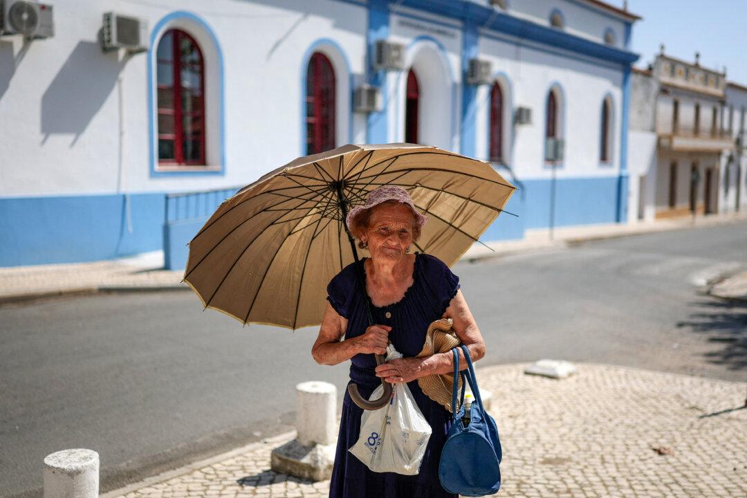 An elderly woman carries an umbrella outside a shop at the village of Amareleja in Alentejo, Portugal, on Aug. 5, 2025. Temperatures above 40 degrees Celsius (104 degrees Fahrenheit) are expected in the interior of the country today. (Patricia De Melo Moreira/AFP via Getty Images)