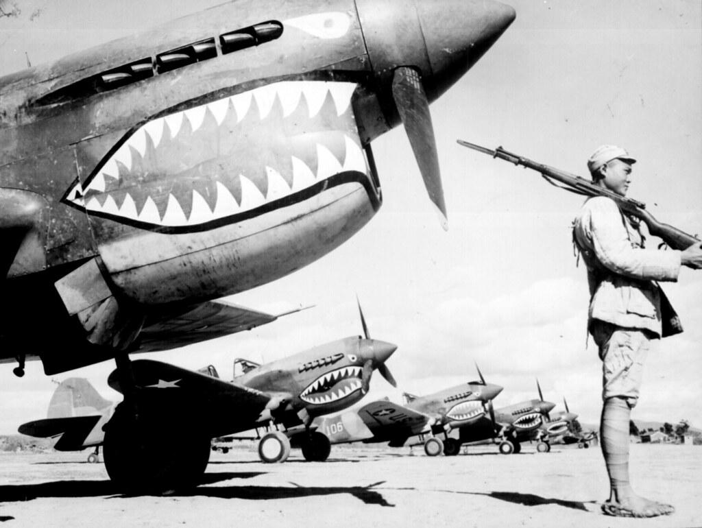 A Chinese soldier guards a line of American P-40 fighter planes, painted with the shark-face emblem of the "Flying Tigers," at a flying field somewhere in China, circa 1942. (Public Domain)