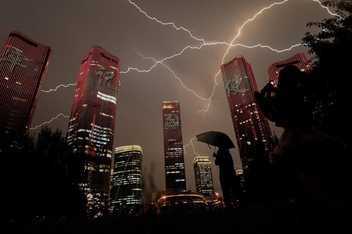 A bolt of lightning crosses the sky as people look at buildings displaying a light show on the eve of the 100th anniversary of the Chinese Communist Party in Beijing on June 30, 2021. (Noel Celis/AFP via Getty Images)
