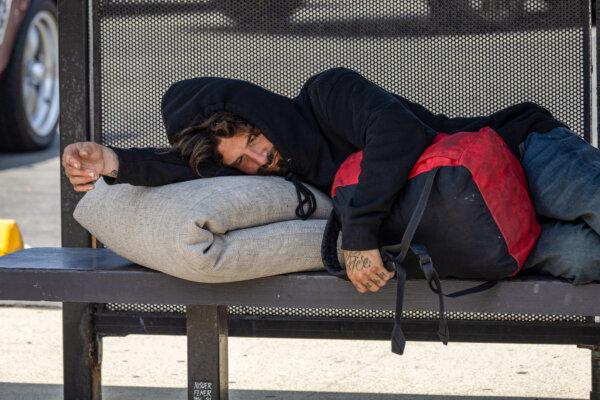A man sleeps at a bus stop in Los Angeles on June 27, 2025. (John Fredricks/The Epoch Times)