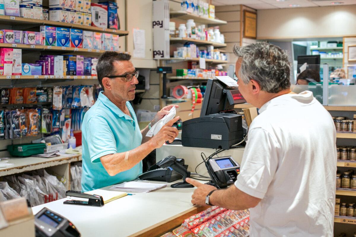 A sales clerk helps a man with his prescription drugs at a pharmacy in New York City on June 18, 2014. (The Epoch Times)