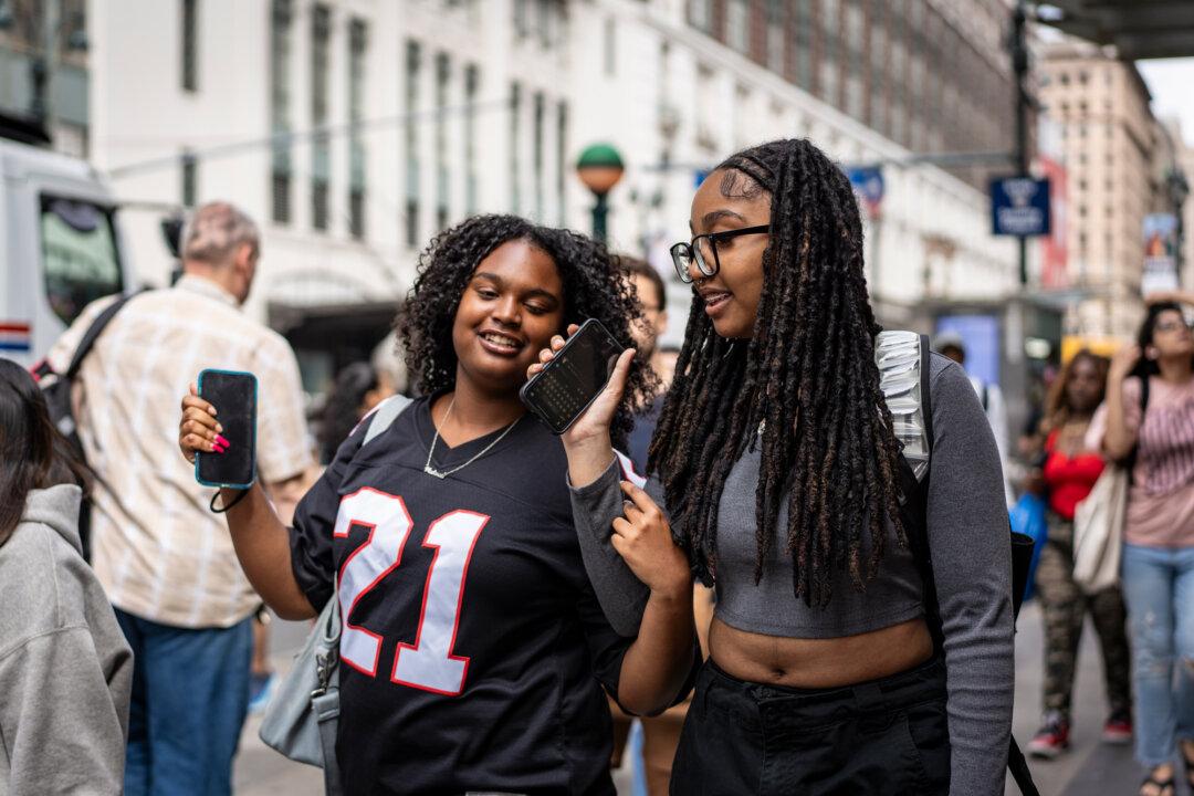 Women with their cell phones in New York City on June 10, 2024. Experts say social media serves as a forum for groups promoting violence, despite platform restrictions. (Samira Bouaou/The Epoch Times)