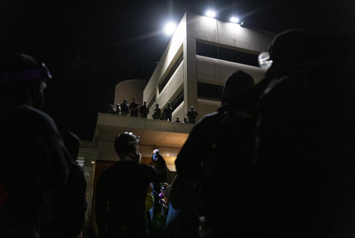 Protesters stand in the dark in front of Immigration and Customs Enforcement offices in Portland, Ore., on Oct. 3, 2025. (John Fredricks/The Epoch Times)