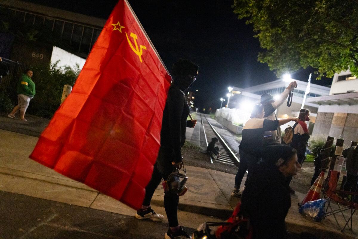 A woman carries a communist flag in front of Immigration and Customs Enforcement offices in Portland, Ore., on Oct. 4, 2025. (John Fredricks/The Epoch Times)