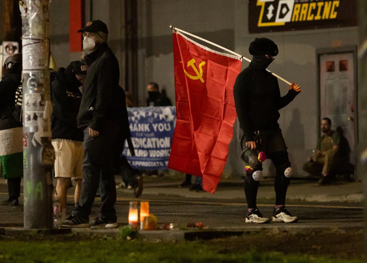 A woman carries a communist flag in front of Immigration and Customs Enforcement offices in Portland, Ore., on Oct. 4, 2025. (John Fredricks/The Epoch Times)