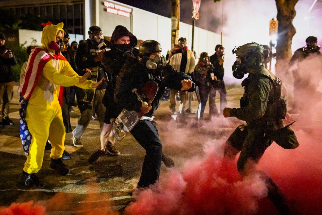 An Antifa demonstrator kicks a smoke bomb back toward federal officers outside Immigration and Customs Enforcement offices in Portland, Ore., on Oct. 5, 2025. (John Fredricks/The Epoch Times)