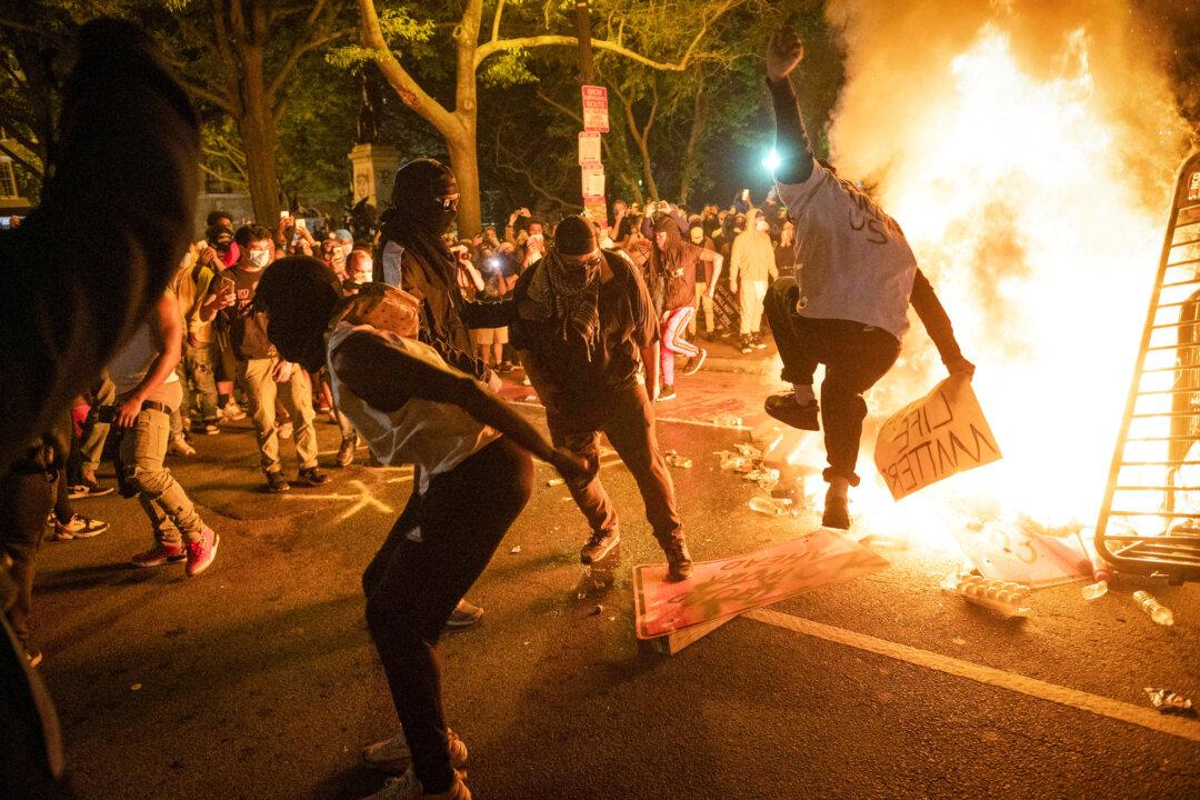 Protesters jump on a street sign near a burning barricade during a riot over the death of George Floyd, near the White House on May 31, 2020. Public awareness of Antifa surged that summer as some of its members aligned with Black Lives Matter demonstrations. (Robert Schmidt/AFP via Getty Images)