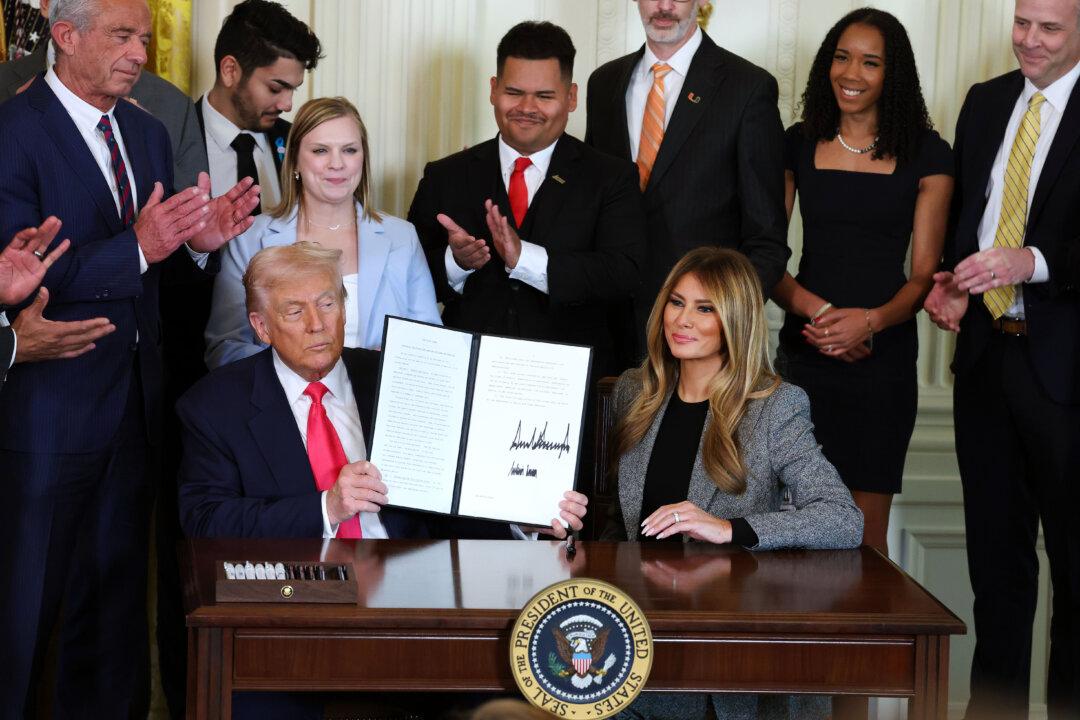 President Donald Trump, joined by First Lady Melania Trump, members of his administration, and foster care advocates, holds up a copy of the “Fostering the Future” executive order after signing the order in the East Room of the White House in Washington on Nov. 13, 2025. The executive order, championed by the first lady, works to expand opportunities for education, career development, housing, and other resources for youth transitioning from foster care to adulthood. (Anna Moneymaker/Getty Images)