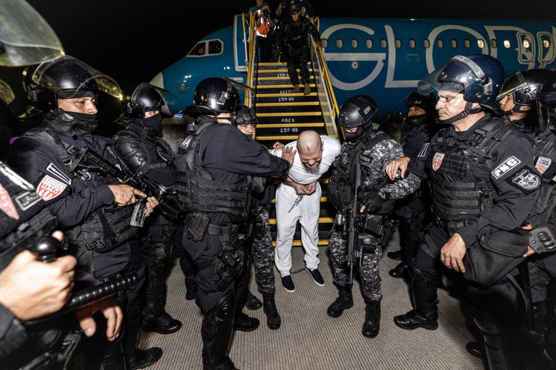 Guards escort a newly admitted inmate, allegedly linked to criminal organizations, at the Terrorist Confinement Center in Tecoluca, El Salvador, on March 16, 2025. Courts are weighing Trump’s deportation plans, which use the 1798 Alien Enemies Act to expedite removals of criminals and members of the Venezuelan gang Tren de Aragua. (Salvadoran Government via Getty Images)