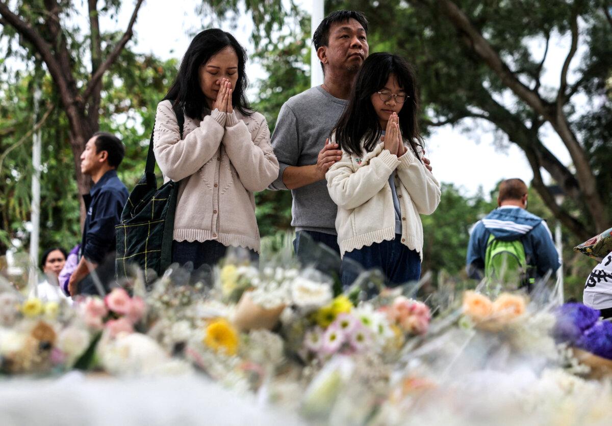 People pray as they come to lay flowers at the makeshift memorial to the victims of the Wang Fuk Court housing complex's deadly fire in Tai Po, Hong Kong, on Nov. 30, 2025. (Maxim Shemetov/Reuters)