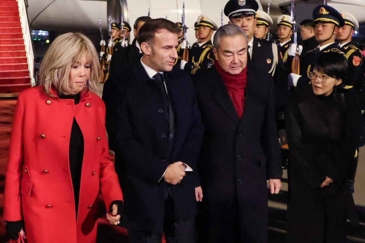 China's Foreign Minister Wang Yi (2nd R) receives France's President Emmanuel Macron (2nd L) and his wife Brigitte Macron (L) upon their arrival at the Capital International Airport in Beijing on Dec.3, 2025. (Ludovic Marin/POOL/AFP via Getty Images)