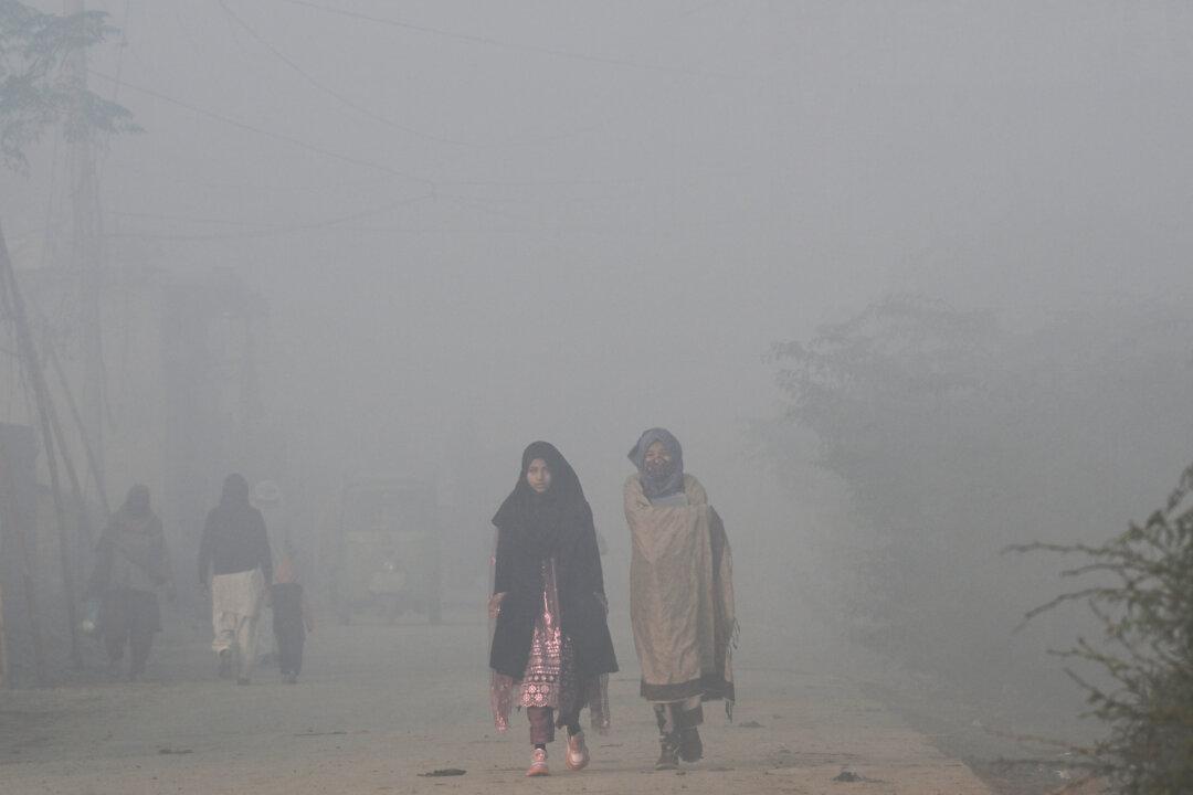 A masked woman walks amid dense smog in Lahore, Pakistan, on Dec. 3, 2025. (Arif Ali/AFP via Getty Images)