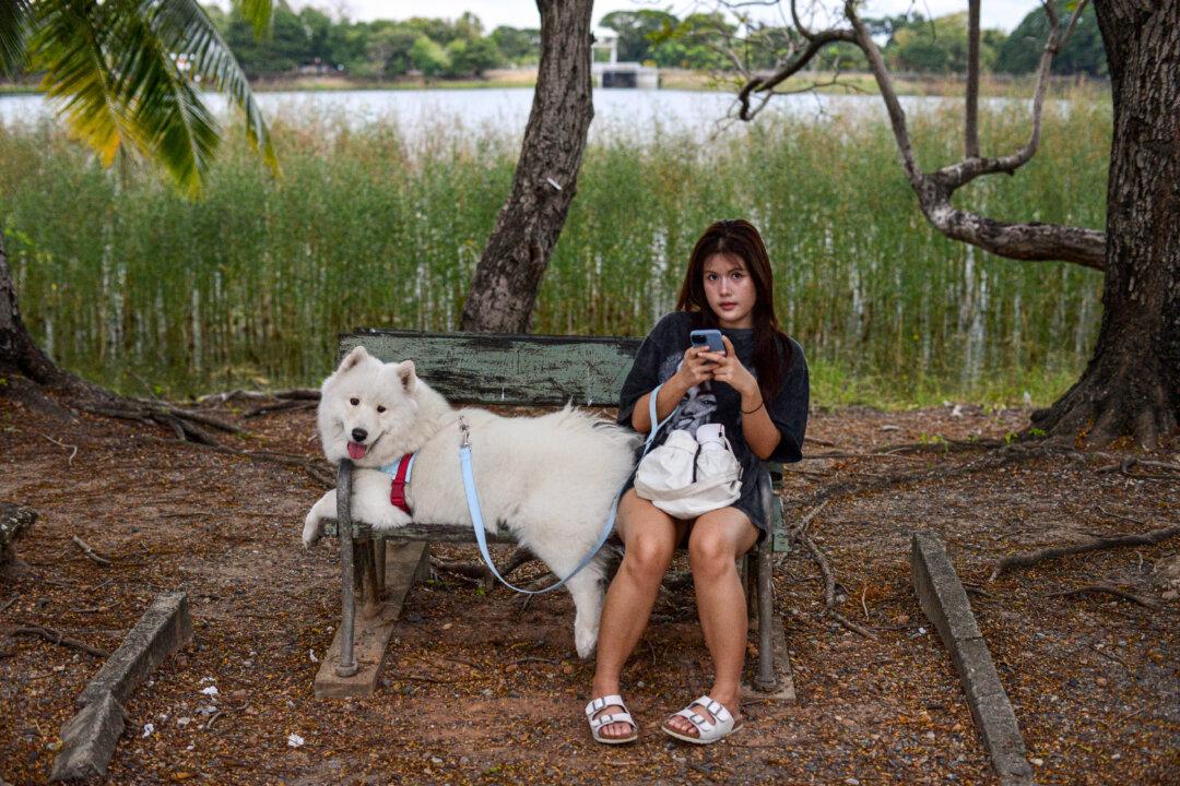 A woman looks on as she sits with her dog on a bench at Nong Bon Lake Park in Bangkok on Dec. 4, 2025. (Amaury Paul/AFP via Getty Images)