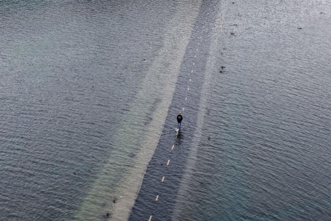 A pedestrian walks along a bike path flooded with seawater during a king tide event in Mill Valley, Calif., on Dec. 5, 2025. The San Francisco Bay Area coast is experiencing some of the highest tides of the year, commonly referred to as a king tide. (Justin Sullivan/Getty Images)