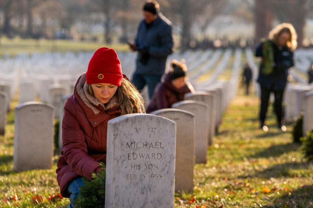 A participant lays a wreath against a headstone on Wreaths Across America Day at Arlington National Cemetery in Arlington, Va., on Dec. 13, 2025. Thousands of participants gathered before sunrise Saturday morning for the annual holiday season event honoring fallen service members. (Allison Robbert/Getty Images)