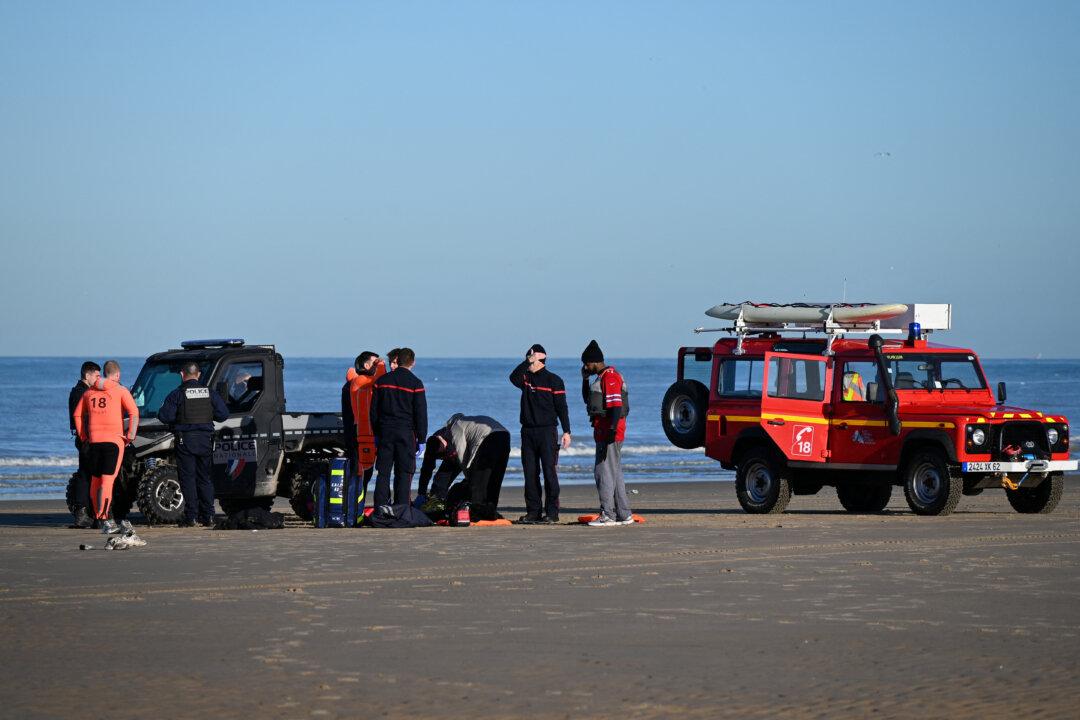 Migrants receive medical care from French firefighters next to police officers after being rescued following their unsuccessful attempt to cross the English Channel in a inflatable boat on a beach in Sangatte, France, on Dec. 13, 2025. (Bernard Barron/AFP via Getty Images)