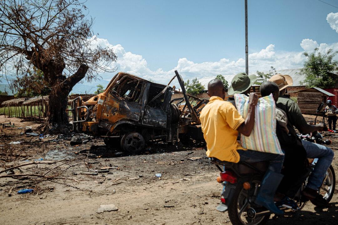 Men on motorcycles coming from Kigubhe, where they had taken refuge, drive past a charred military vehicle belonging to the Armed Forces of the Democratic Republic of Congo as they return to Togota after waiting for calm to be restored in their region in Luvungi, on Dec. 13, 2025. (Jospin Mwisha/AFP via Getty Images)