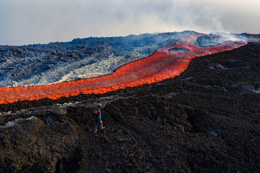 A man stands near a flow of lava on the Mount Etna volcano in Italy on Aug. 28, 2025. The Etna volcanic eruption started on Aug. 10 and remained active for weeks. (Giuseppe Distefano/AFP via Getty Images)