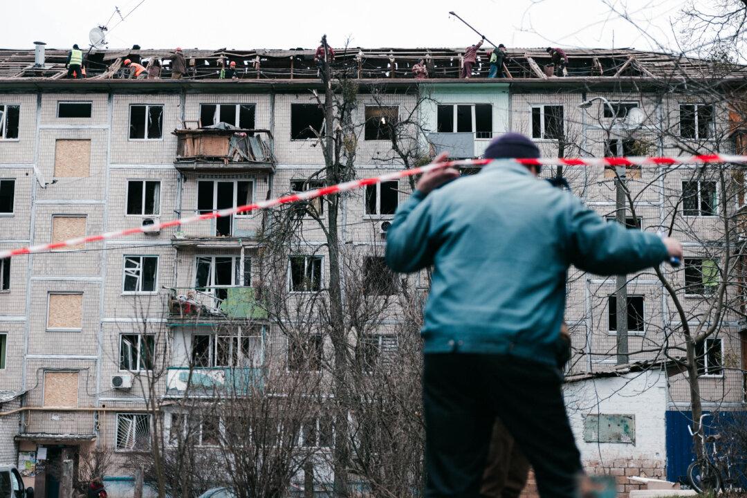 A man lifts red and white tape cordoning off a residential building hit by a Russian air strike while others clean the roof in the Sviatoshynskyi district of Kyiv, Ukraine, on Dec. 23, 2025. The attack partially damaged the building's roof and facade, injuring four people. (Daniel Yovkov/Hans Lucas/AFP via Getty Images)