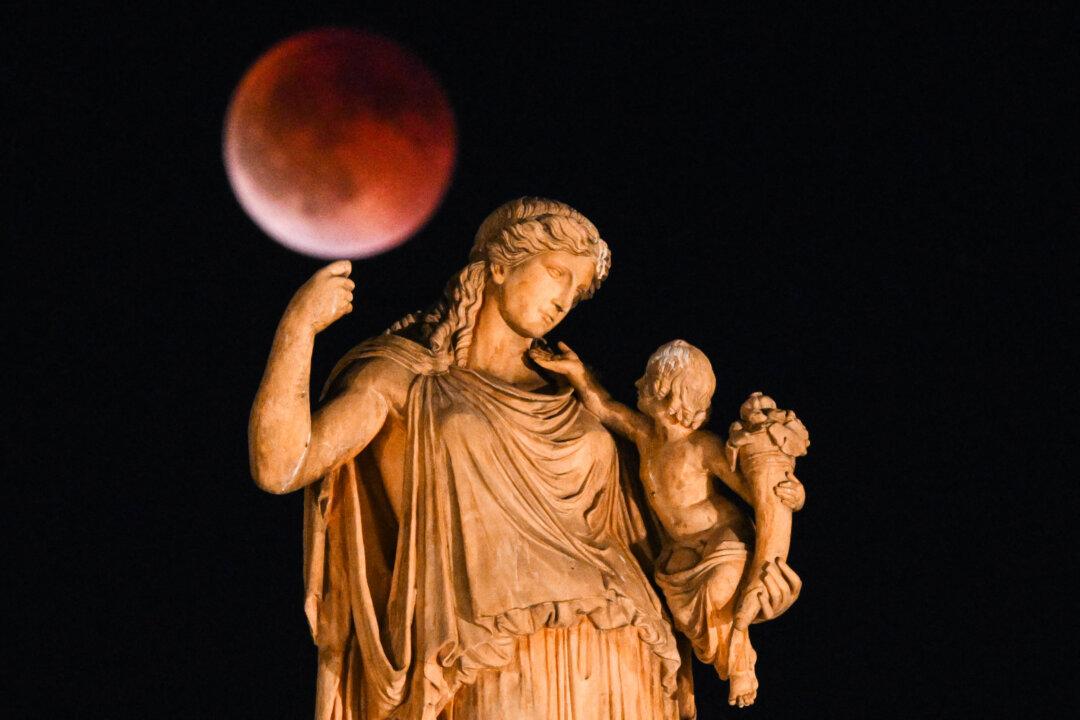A full moon during a lunar eclipse, also known as a Blood Moon, with a statue of the ancient Greek goddess Irene holding a child in the foreground, in central Athens, Greece, on Sept. 7, 2025. (Angelos Tzortzinis/AFP via Getty Images)