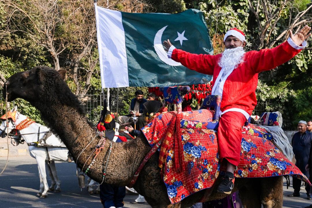 A volunteer dressed as Santa Claus gestures next to Pakistan's national flag as he rides a camel during a Christmas peace rally in Lahore, Pakistan, on Dec. 23, 2025. (Arif Ali/AFP via Getty Images)