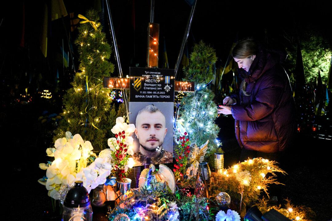 A woman arranges a Ukrainian soldier's grave, adorned with Christmas trees and New Year's decorations, at the Lychakiv Military Cemetery in Lviv, Ukraine, on Dec. 23, 2025. (Yuriy Dyachyshyn/AFP via Getty Images)