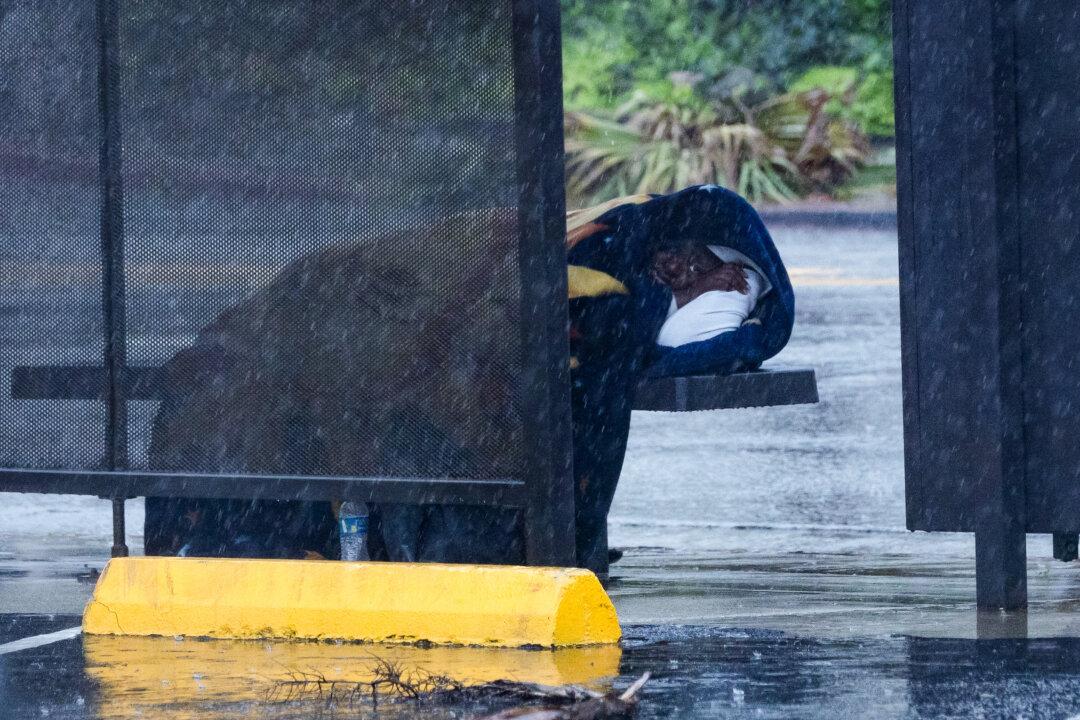 A person shelters from a rainstorm at a bus stop in Los Angeles on Dec. 24, 2025. (John Fredricks/The Epoch Times)