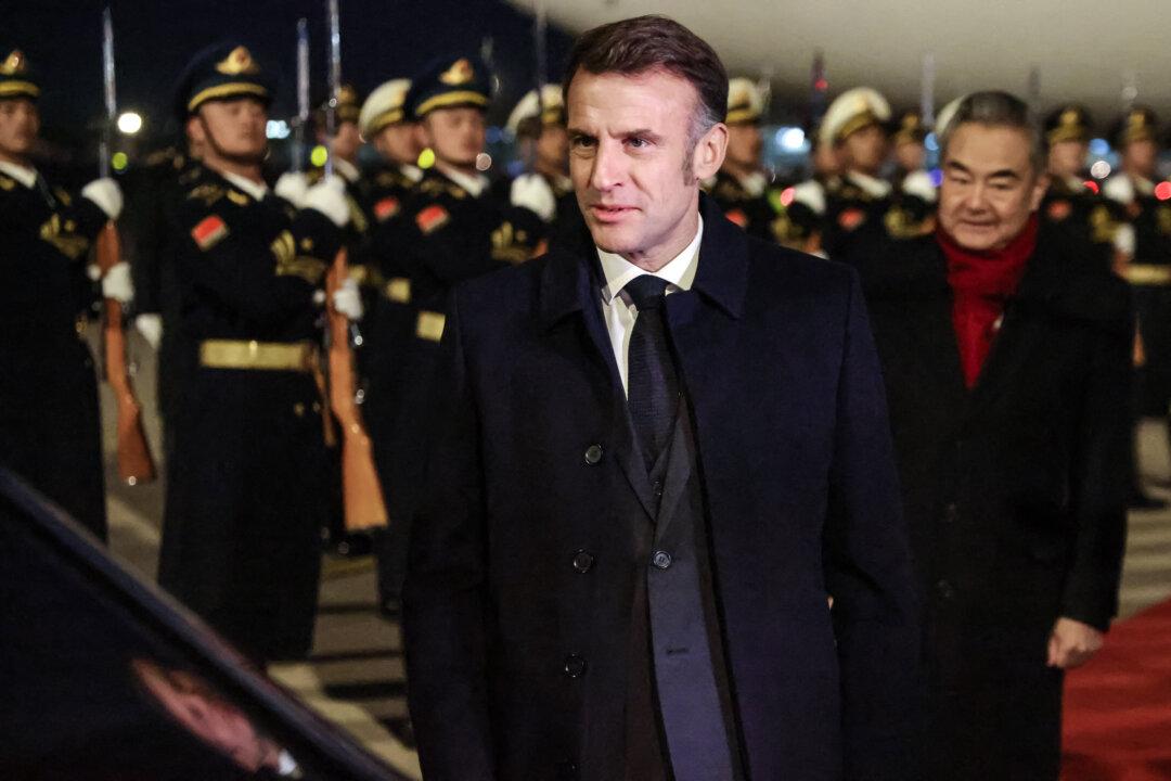 China’s Foreign Minister Wang Yi (R) walks behind French President Emmanuel Macron to his vehicle at Capital International Airport in Beijing on Dec. 3, 2025. Macron said earlier this month that Europe could be forced to take “strong measures,” including tariffs, if Beijing does not address the EU’s widening trade imbalance with China. (Ludovic Marin-Pool/Getty Images)