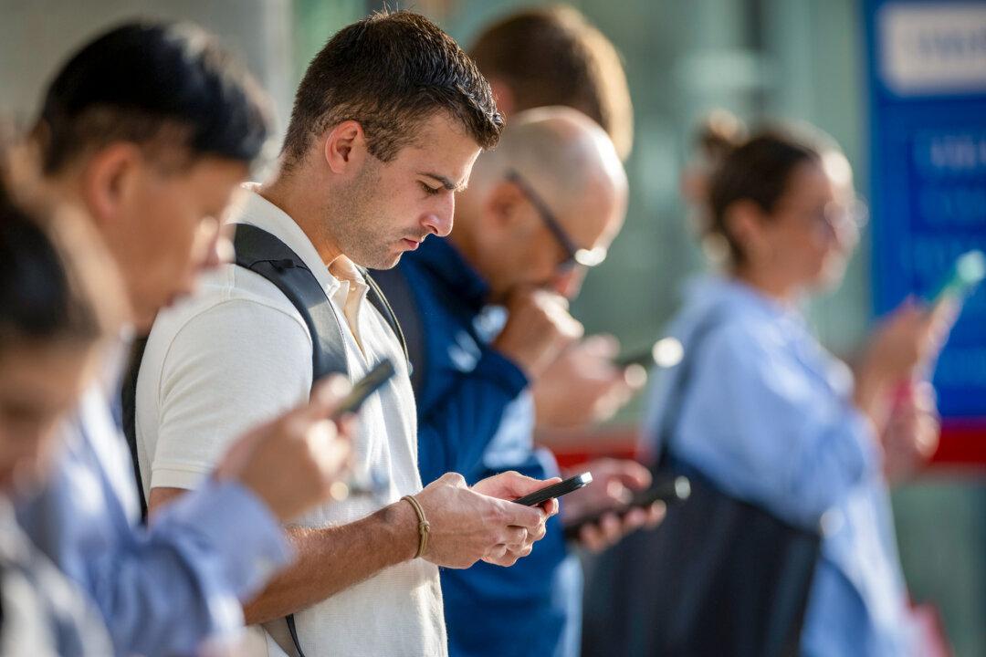 People check their phones while waiting for the train to arrive in Stamford, Conn., on Aug. 28, 2023. Americans spend an average of 5 hours and 16 minutes a day on their phones, according to a 2025 report by Harmony Healthcare IT. (John Moore/Getty Images)