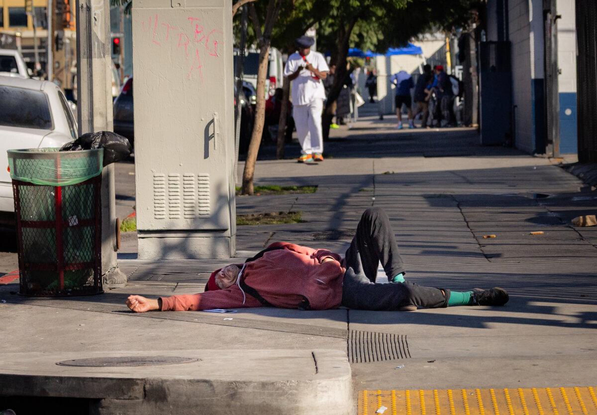 A homeless individual lies on a sidewalk in Los Angeles on Jan. 7, 2026. (John Fredricks/The Epoch Times)