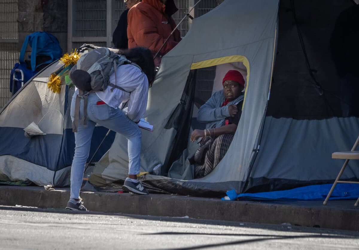 People approach a woman resting in a homeless encampment in Los Angeles, on Jan. 7, 2026. (John Fredricks/The Epoch Times)