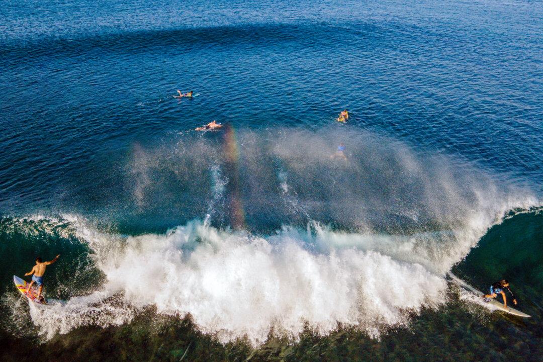 Surfers ride a wave in Lhoknga Beach, Indonesia's Aceh province, on Jan. 12, 2026. (Chaideer Mahyuddin/AFP via Getty Images)