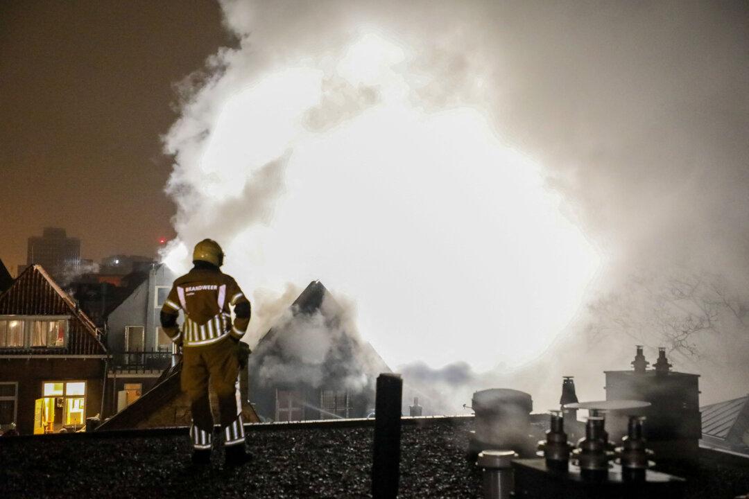 A firefighter looks at smoke from a fire raging in a house on Grote Hoogstraat in the historic city center of Leeuwarden, Netherlands, early on Jan. 13, 2026. The Friesland Safety Region reports that the top floor and roof are engulfed in flames, and the fire has spread to adjacent buildings. (Anton Kappers/ANP/AFP via Getty Images)