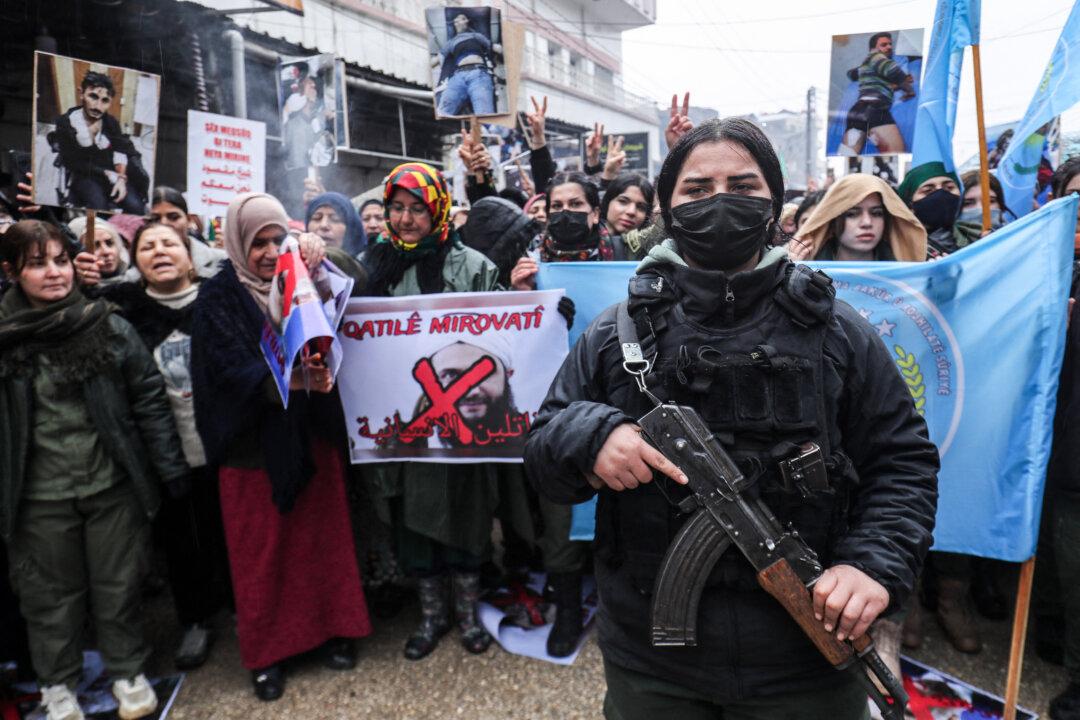 A member of the Kurdish security forces stands guard as Syrian Kurds hold a portrait of Syrian President Ahmed al-Sharaa that reads “Killers of Humanity” at a demonstration in the Kurdish-controlled northeastern city of Qamishli, on Jan. 13, 2026. They are protesting violence they say was committed by Syrian government forces during recent clashes in Aleppo's Kurdish neighborhoods. (Delil Souleiman/AFP via Getty Images)