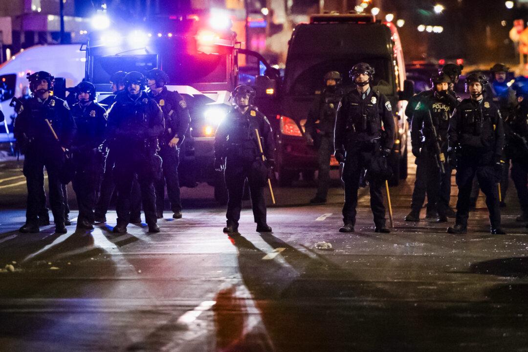 (Top) Protesters demonstrate against federal immigration operations in front of police officers in Minneapolis on Jan 9, 2026. (Bottom) Law enforcement officers stand in formation during a protest against ICE operations in Minneapolis on Jan. 9, 2026. (John Fredricks/The Epoch Times)