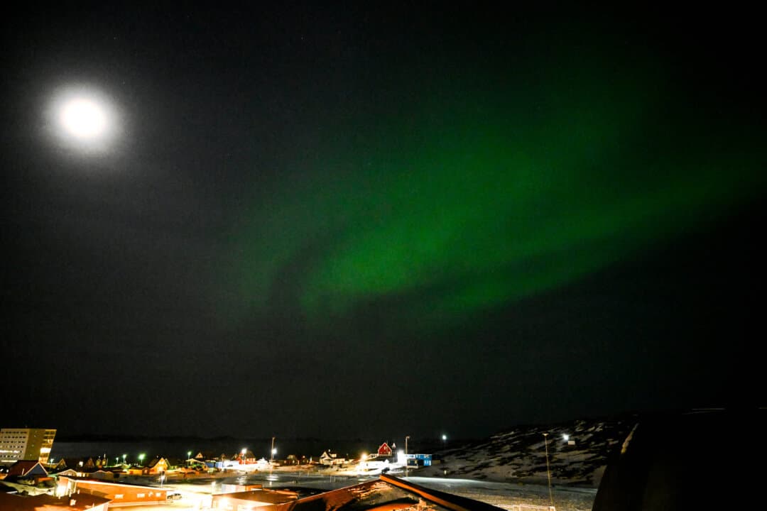 The northern lights glow and the moon shines in the night sky over Nuuk, Greenland, on Jan. 26, 2026. (Ina Fassbender / AFP via Getty Images)
