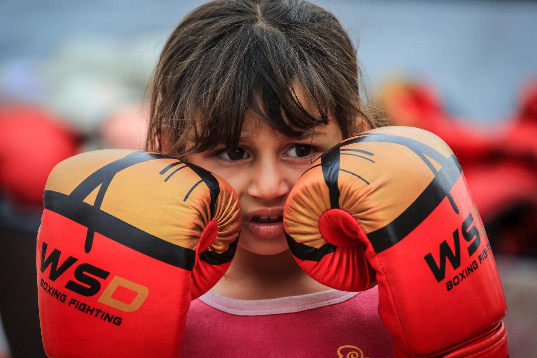 A Palestinian girl holds her boxing gloves up to her face during a training session between displacement tents in Khan Yunis, in the southern Gaza Strip, on Feb. 9, 2026. After a long hiatus from training, the women's boxing team—which consists of 45 boxers between the ages of 8 and 19—has resumed its sessions under the guidance of their coach Osama Ayoub. (Bashar Taleb/AFP via Getty Images)