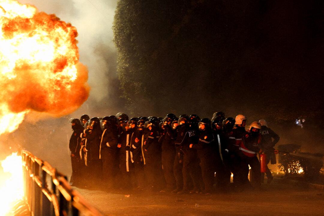 Law enforcement officers stand guard behind crowd-control barriers as a Molotov cocktail explodes outside the Prime Minister's office during an anti-government protest triggered by a corruption investigation into Deputy Prime Minister Belinda Balluku, in Tirana, Albania, on Feb. 10, 2026. (Florion Goga/Reuters)